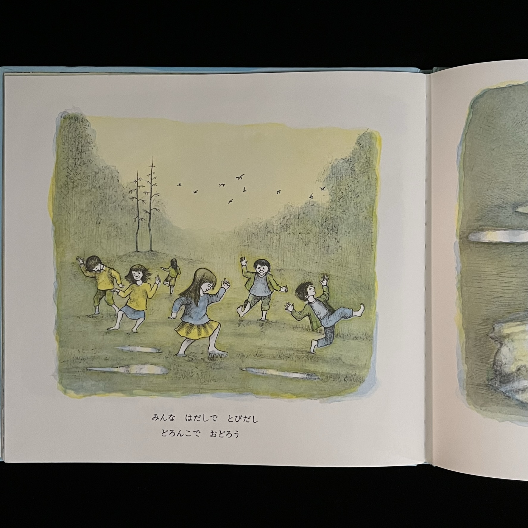 本の中のページの写真。子どもたちが外にでて水たまりのある泥の上で元気にはしゃいでいる