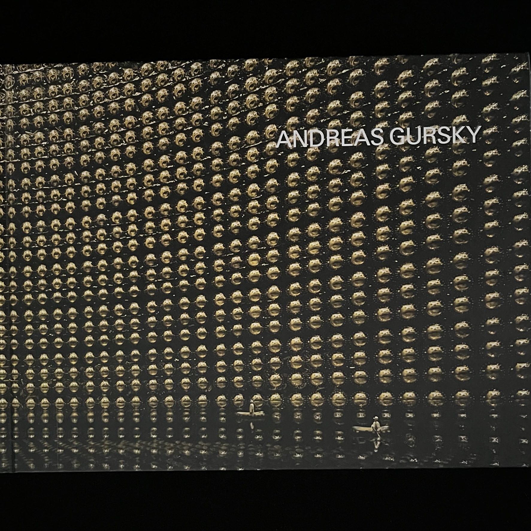 『ANDREAS GURSKY』の写真集の表紙の写真。スーパーカミオカンデのニュートリノの痕跡をとらえる１万個以上の丸い光センサーが壁面びっしり配置されています。床の部分は水がたたえられていて、人が乗った小舟が２艘浮かんでいます。