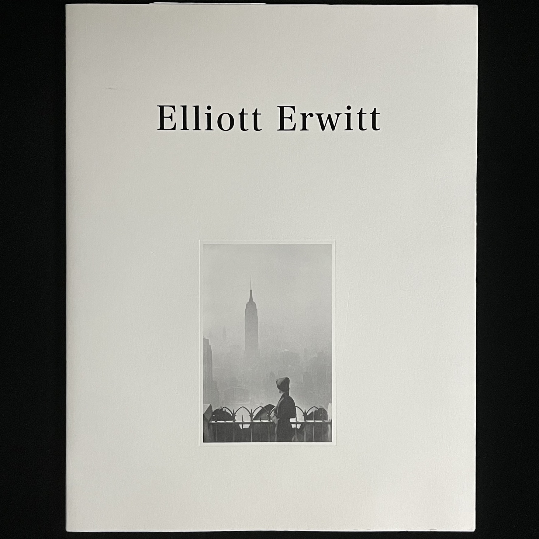 『ELLIOT ERWITT』の写真集の表紙の写真。女性が立つ柵の向こうに霧にかすむエンパイヤ―ステイトビルディングがそびえている写真が載っています。
