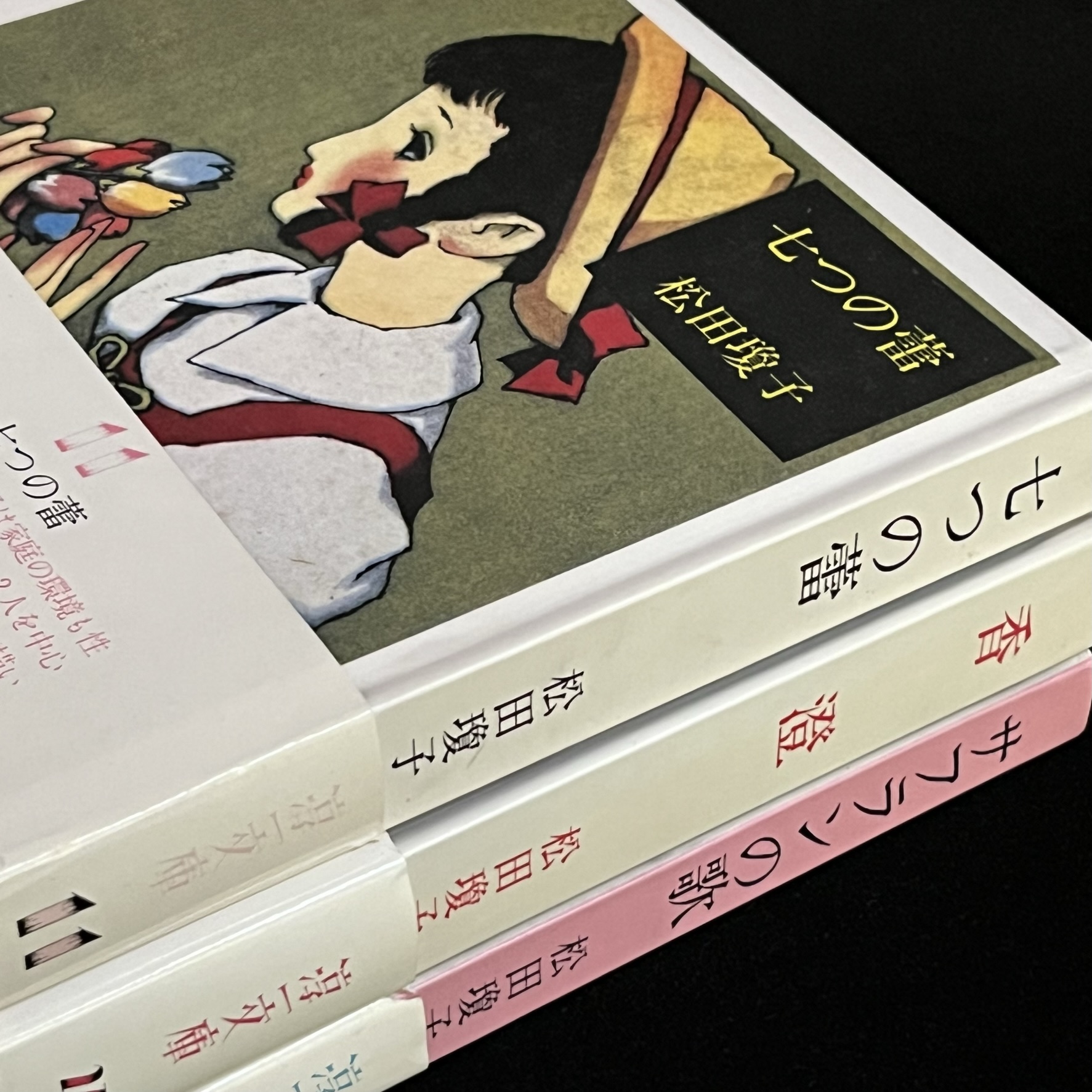松田瓊子さんの３冊の本の写真です。『七つの蕾』『香澄』『サフランの歌』の本です。装画は中原淳一さん。『七つの蕾』の表紙には、帽子をかぶり、三つ編みの髪に赤いリボンをつけた乙女が描かれており、手には色とりどりのお花を７，８輪持っています。